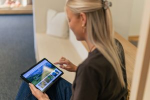 Hotelgast sitzt im Zimmer und bedient einen digitalen Gäste-Account der SoftTec Cloud Hotelsoftware auf einem Tablet per Touchscreen.