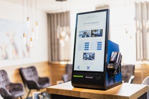 Indoor Self-Check-in-Kiosk von SoftTec Cloud im Hotelfoyer mit Touchscreen-Anzeige der Zimmerkategorien, Preisen und integriertem Kartenlesegerät.