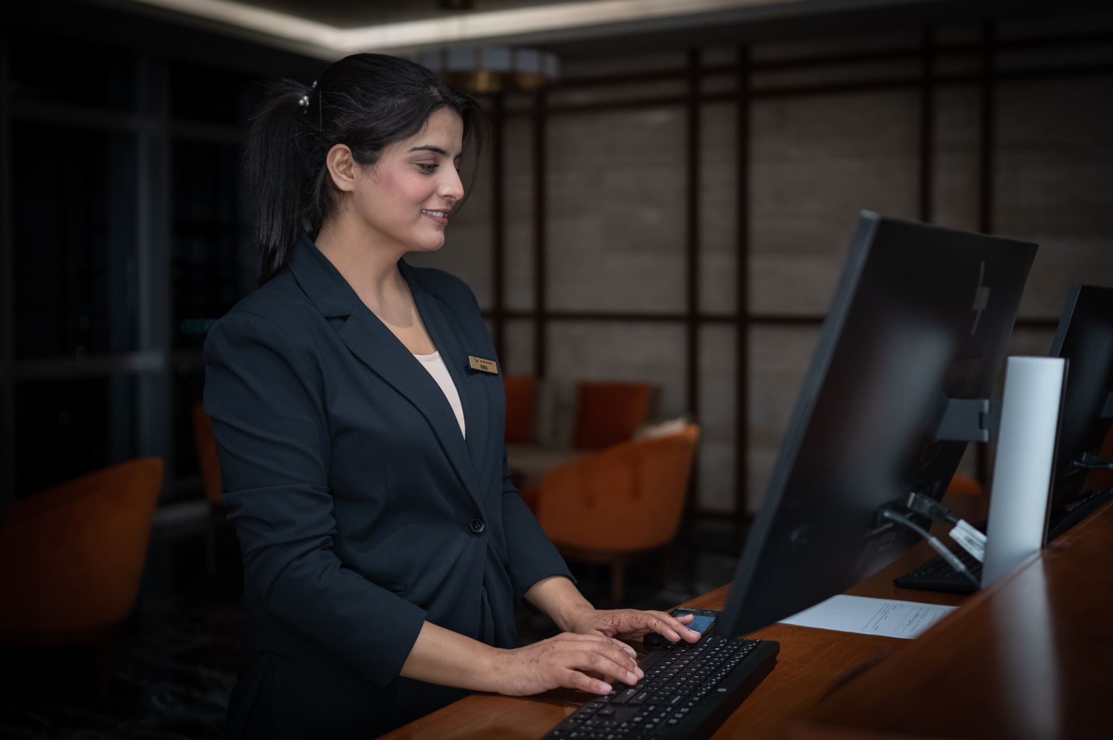 Rezeptionistin in Hotelkleidung arbeitet stehend am Computer an der Hotelrezeption
